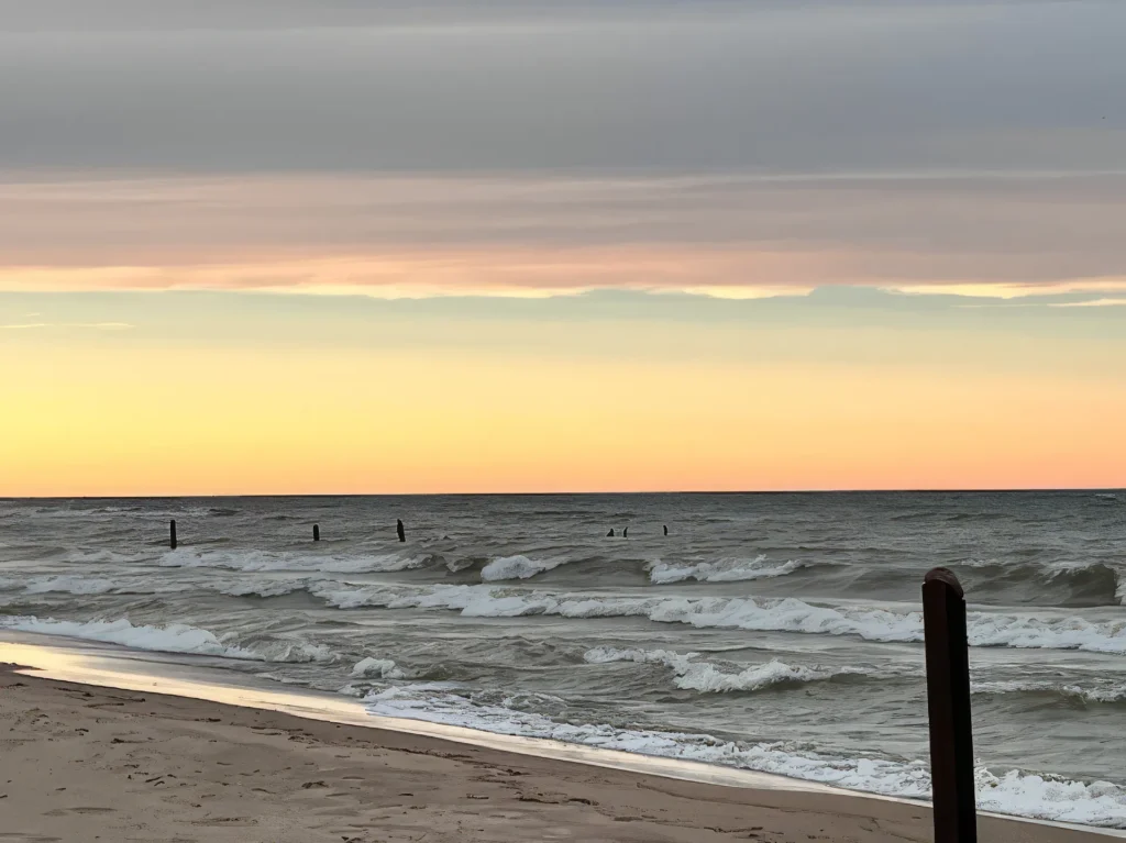 Lake Huron waves rolling onto sandy beach at sunset with wooden posts and dramatic cloudy sky at Forester Park.