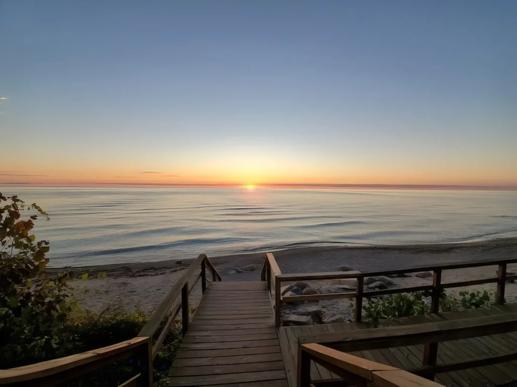 Wooden boardwalk leading to beach at sunset with calm Lake Huron waters and colorful sky at Forester Park.
