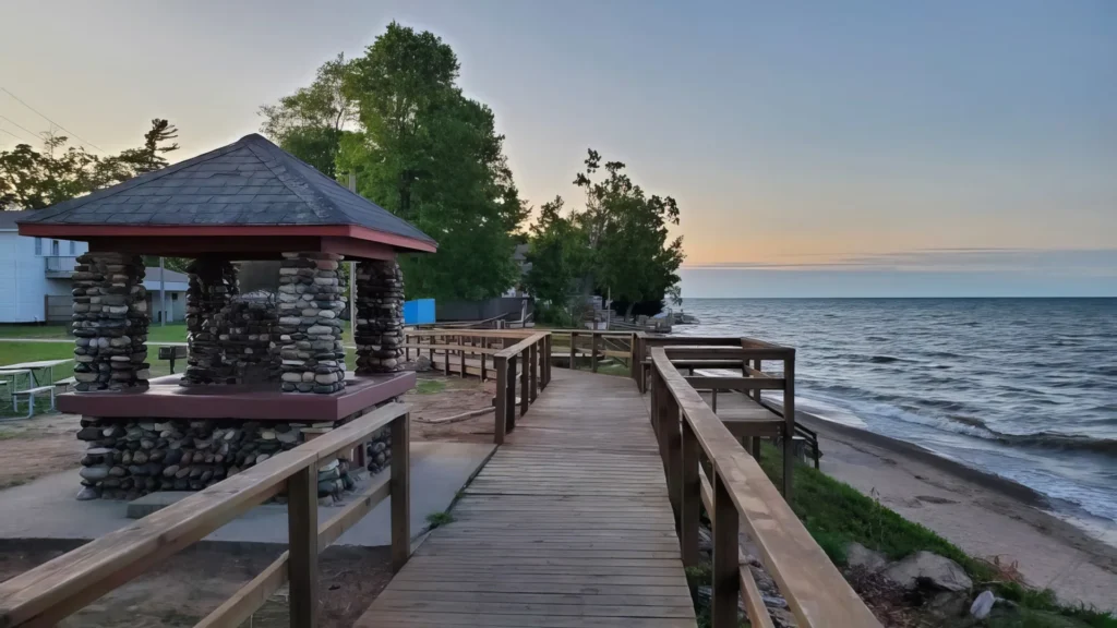 Wooden boardwalk next to a stone water fountain leading to a stone pavilion at lakeside during sunset at Forester Park.