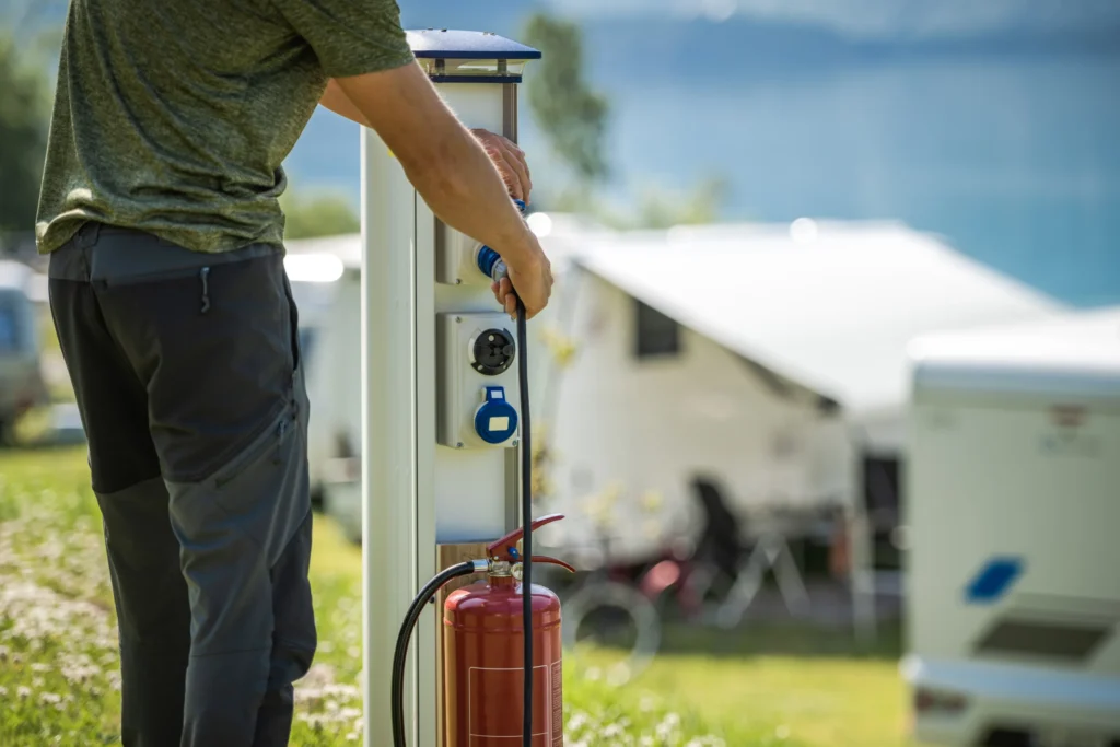 Person plugging an RV power cord into an electrical hookup pedestal at a campsite