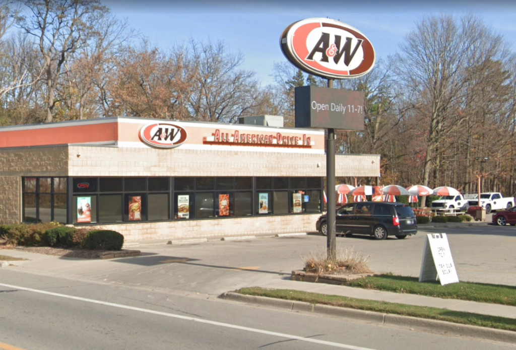 Exterior of an A&W restaurant with a sign reading "Open Daily 11-7" and outdoor seating with red and white umbrellas.