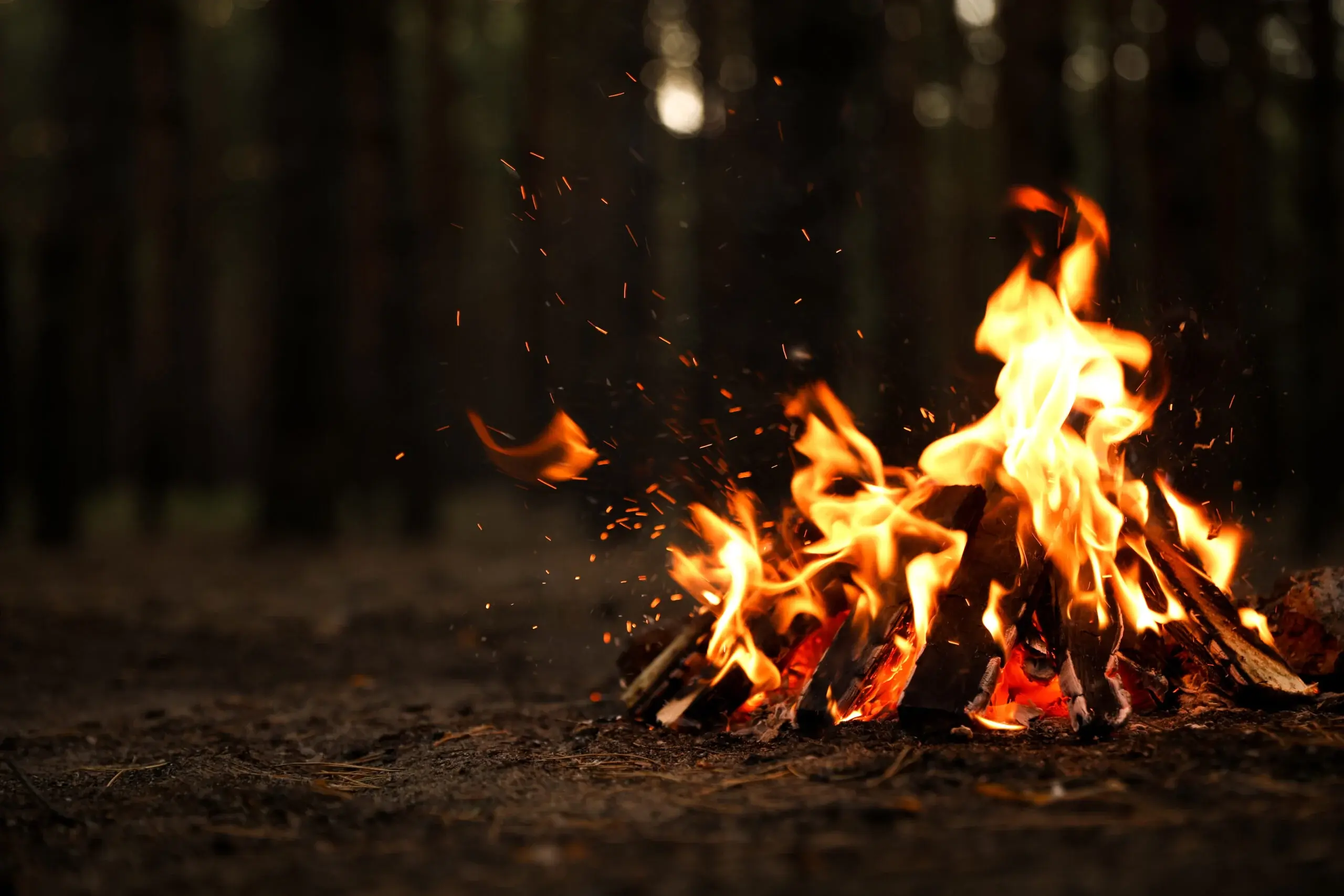Campfire with orange flames and glowing embers against a dark background