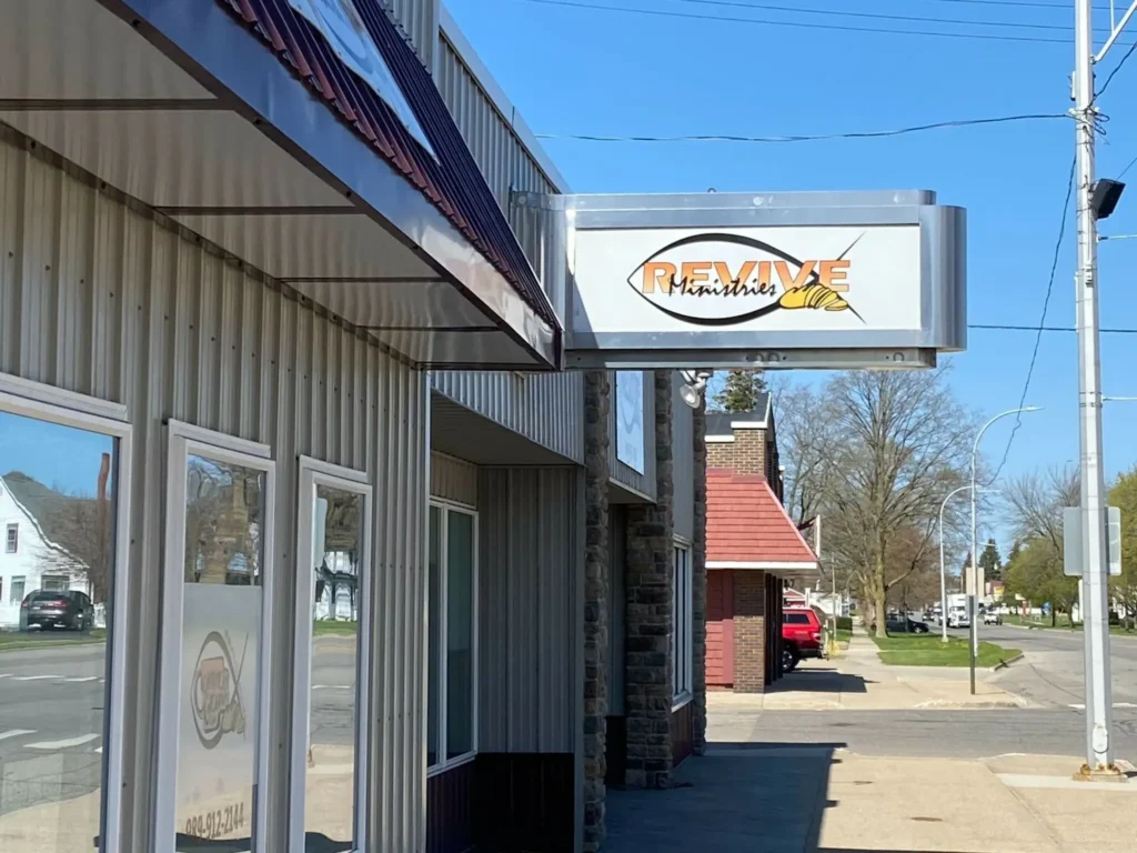 Sign for "Revive Ministries" on a building exterior along a sunny street.