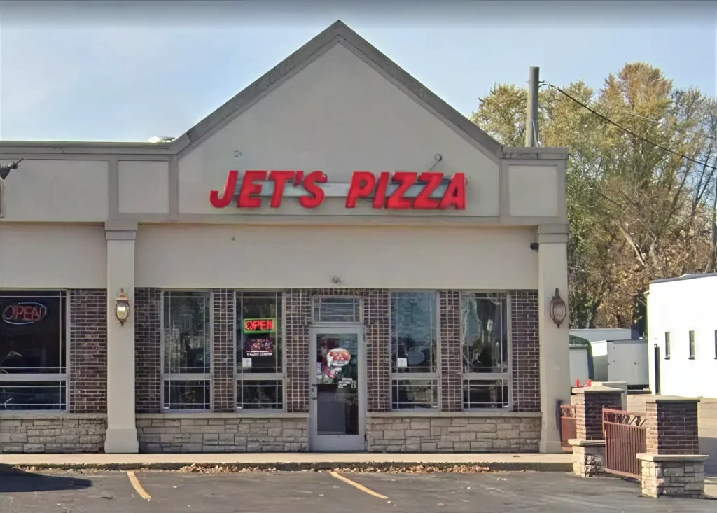 Facade of Jet's Pizza restaurant with a red sign and "Open" neon lights in the windows.