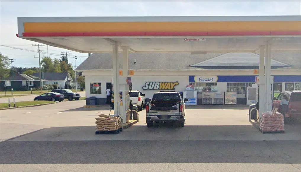 Gas station with a convenience store featuring Subway and Forward signs. Two vehicles parked at the pumps, with bags of goods nearby.