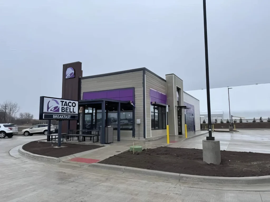 Exterior of a Taco Bell restaurant with a breakfast sign, featuring a modern design and a parking lot.