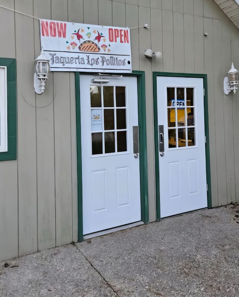 Entrance of Taqueria Los Pollitos with a "Now Open" sign above two white doors.