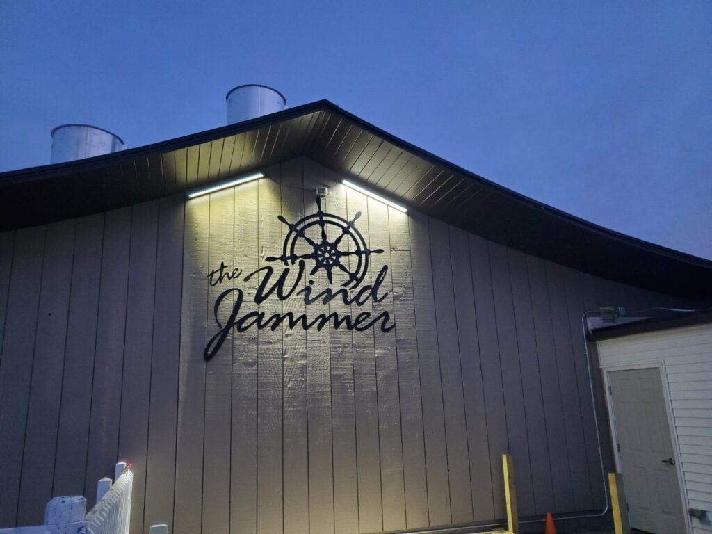 Exterior of a building with the illuminated sign "The Wind Jammer" featuring a ship's wheel design.