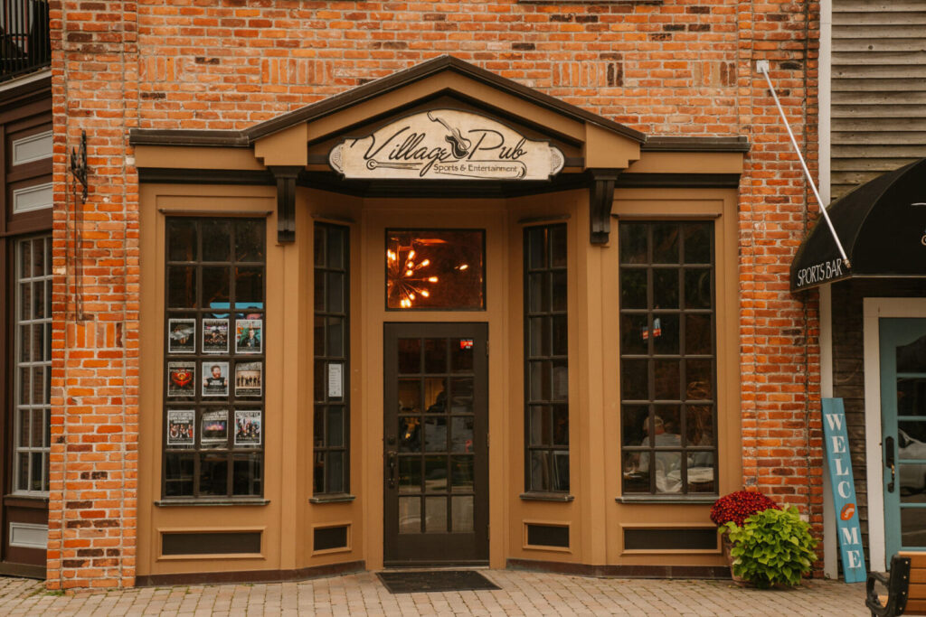 Entrance of Village Pub with brick exterior, large windows, and a "Welcome" sign.