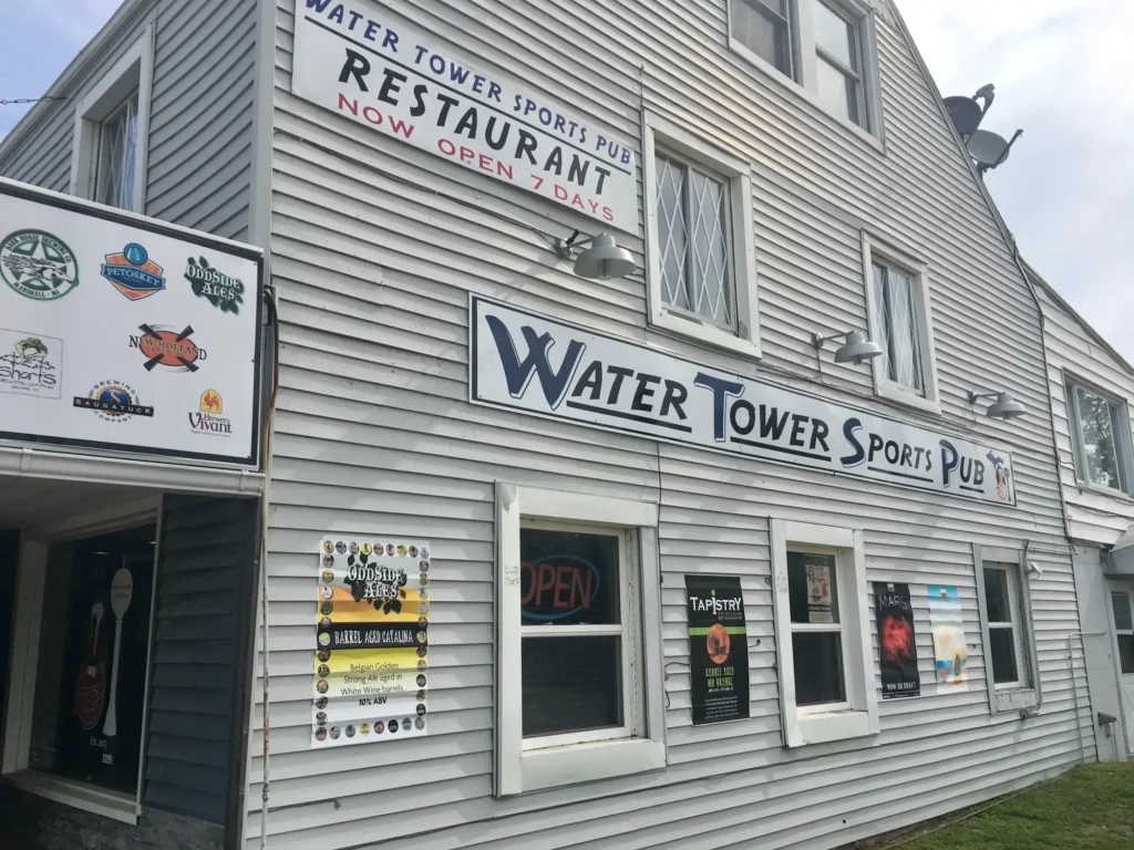 Exterior of Water Tower Sports Pub, a gray building with multiple signs and posters advertising various beers and events.